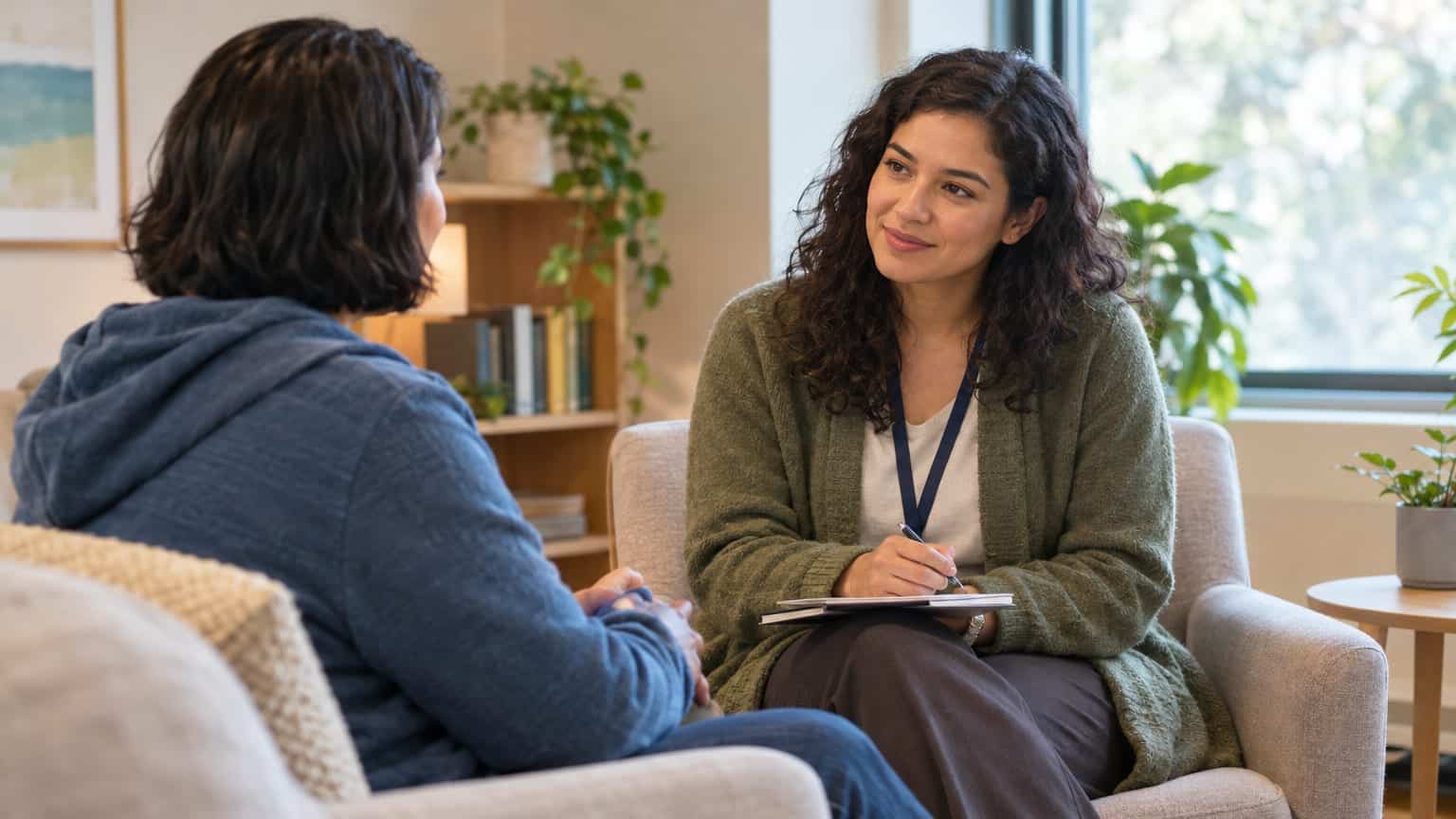 Counselor with notepad listening attentively to a client in a warm therapy office setting